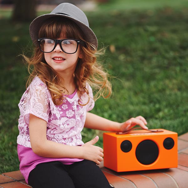 Little hipster girl listening to music on a bluetooth speaker